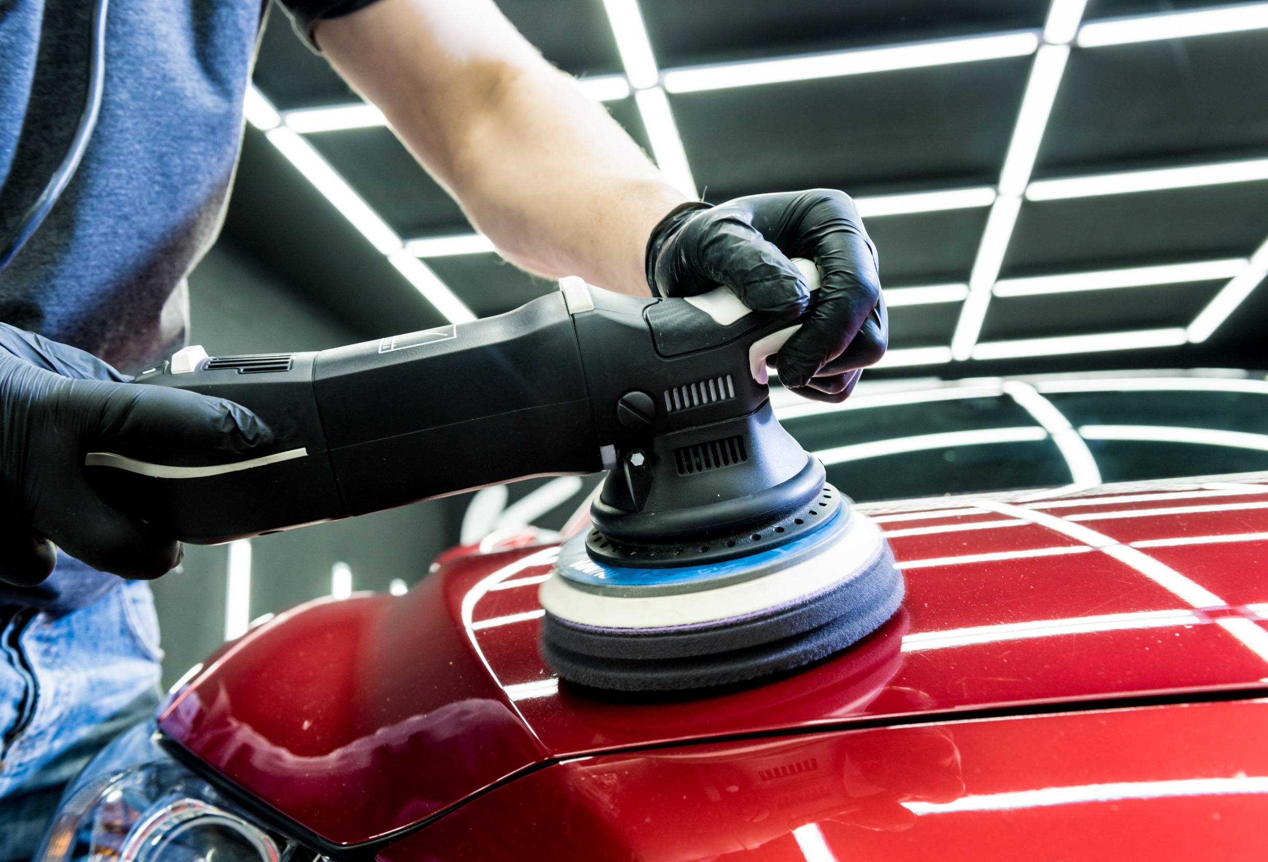 Services car service worker polishes a car details with orbital polisher.